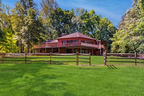 A large, two-story building with a balcony, surrounded by a wooden fence and lush green trees. - Rustic Lakehouse With Views, Kayaks, Wifi, Central AC & Cozy Firepit Nights (Bumpass)