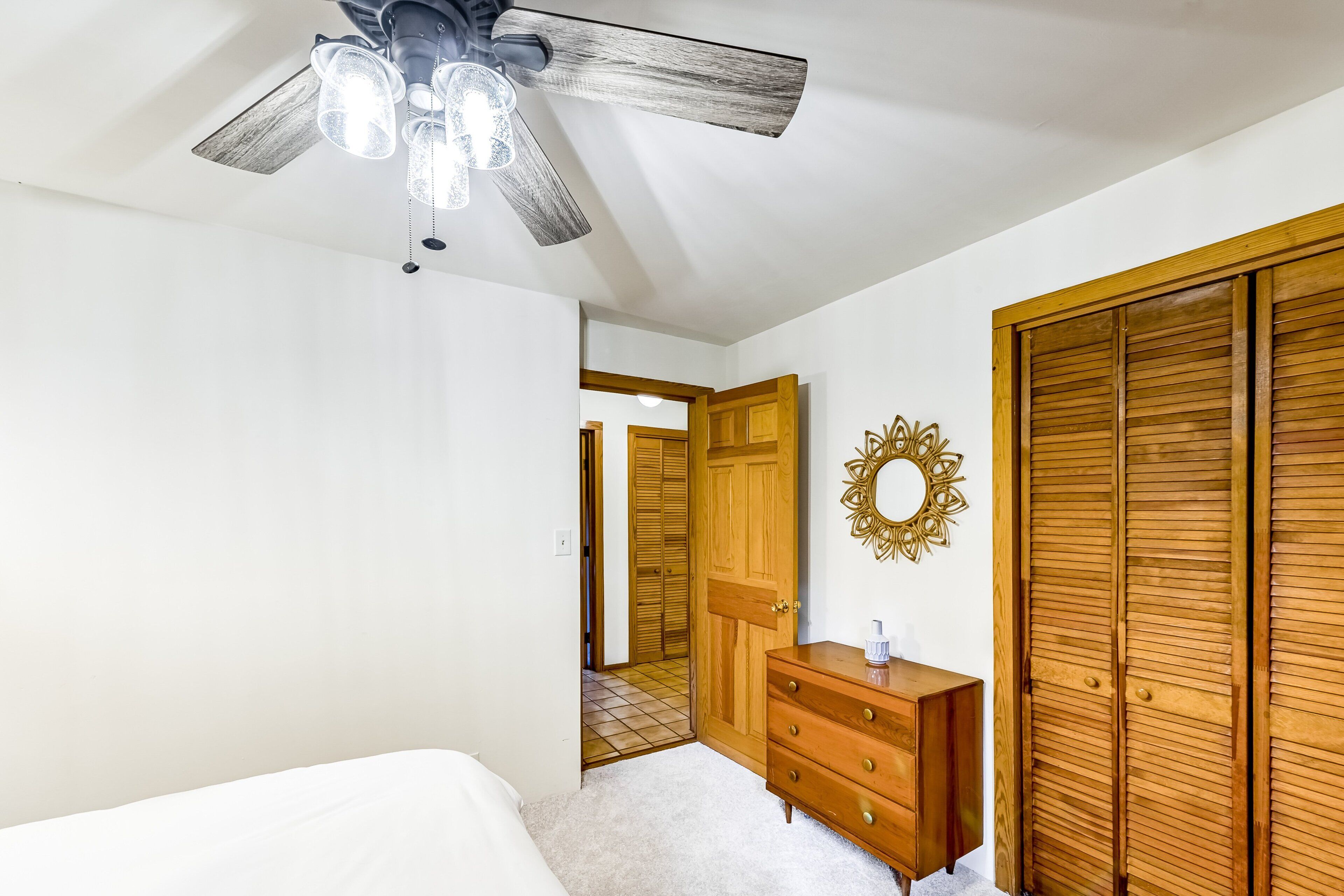 A bedroom with a ceiling fan, wooden wardrobe, dresser, and a mirror on the wall.