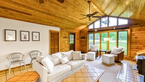 A wooden cabin interior with a sofa, chairs, a table, a ceiling fan, and a fireplace. - Lakeside log Home With a Private Deck, Wifi, Firepit, Central AC, & Washer/dryer (Mineral)