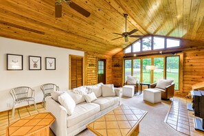 Ein Holzblockhaus-Innenraum mit einer Couch, Stühlen, einem Tisch, einem Deckenventilator und einem Kamin.