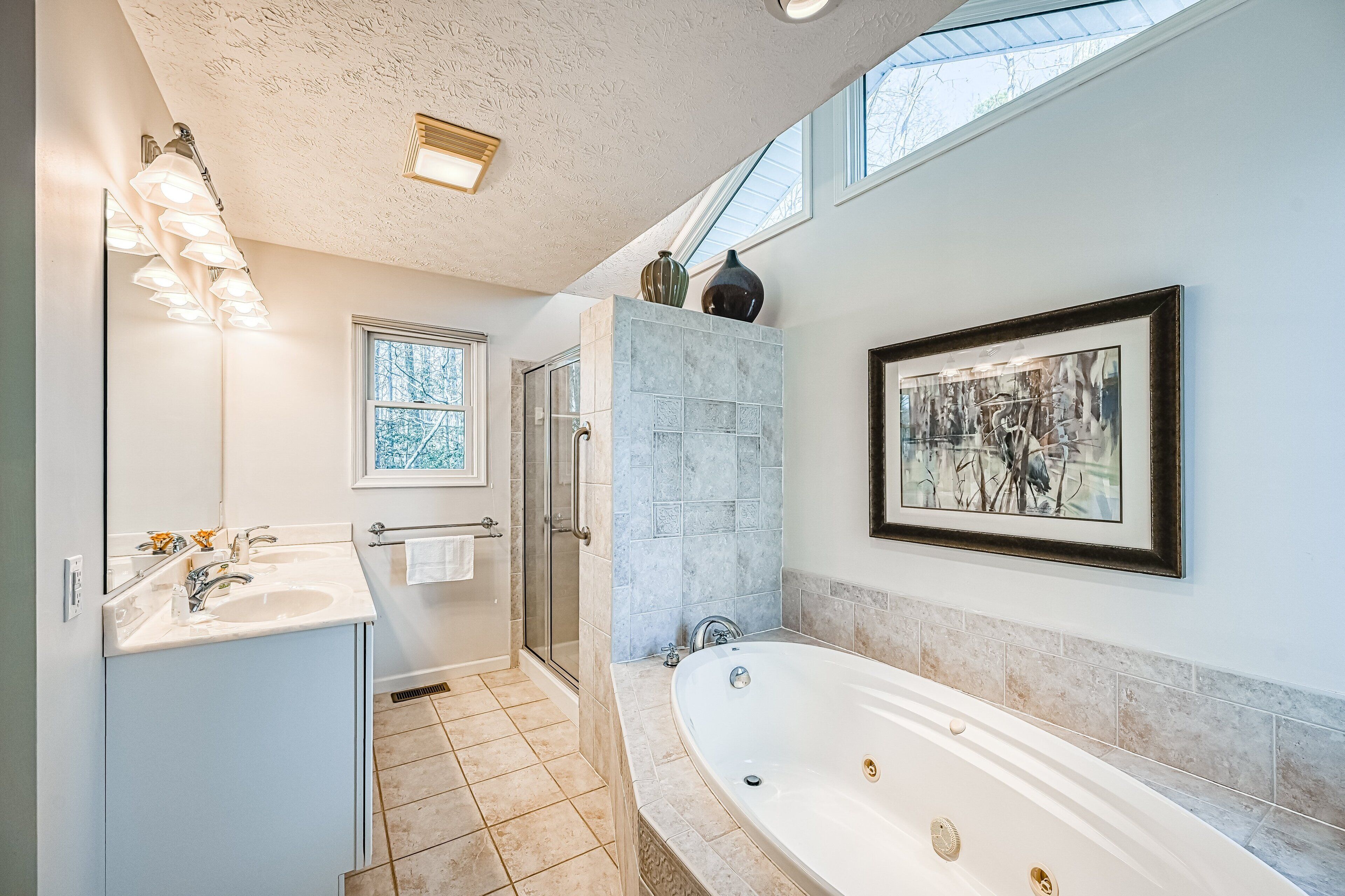 A bathroom with a large bathtub, a shower, a double sink, and a framed artwork on the wall.