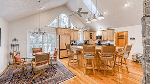 A spacious kitchen with wooden cabinets, a large island, and a dining area with chairs. - Stunning Lakeside Home With Dock, Large Deck, Firepit, Kayaks & Pool Table (Bumpass)