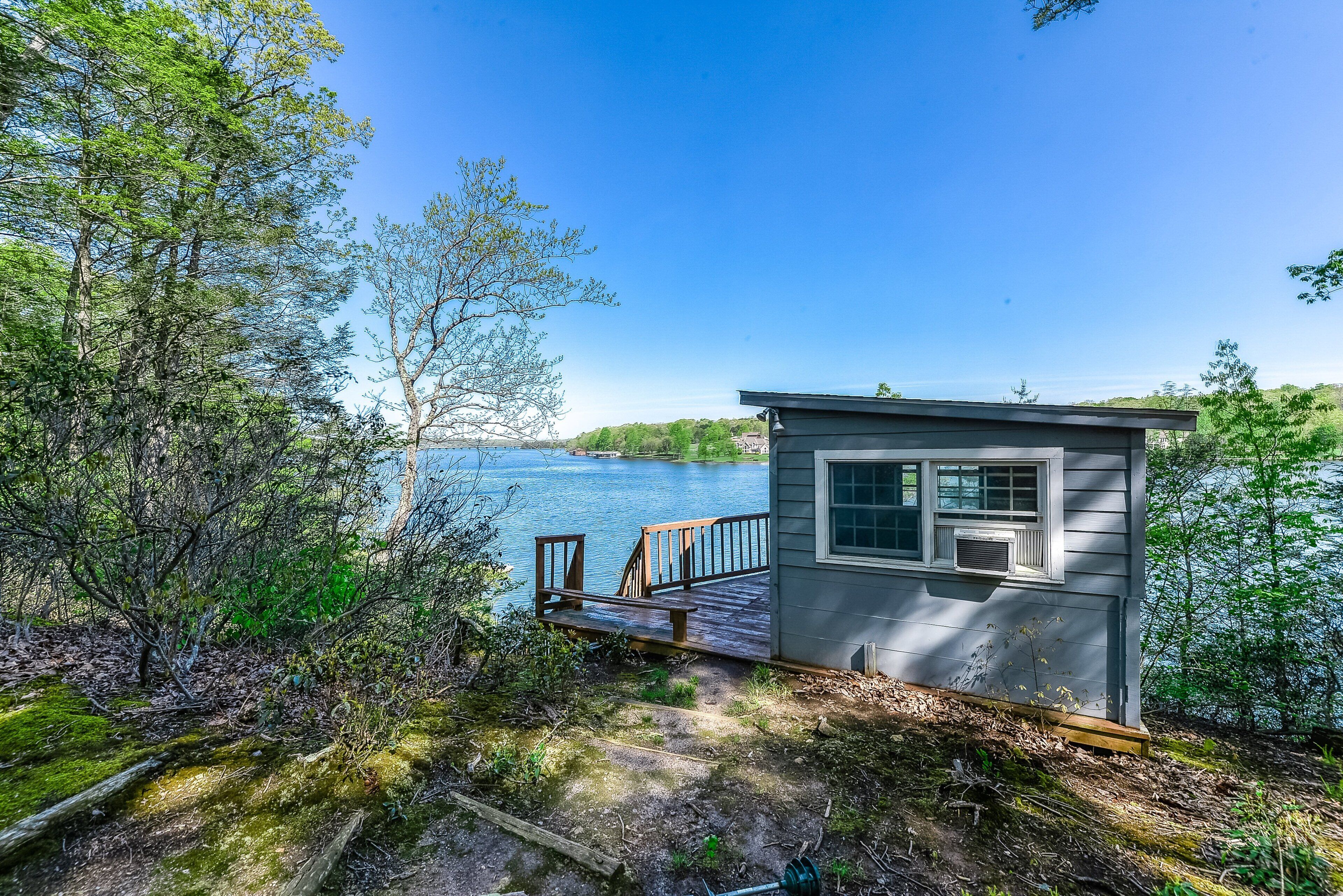 A small cabin with a dock extending into a lake, surrounded by trees.