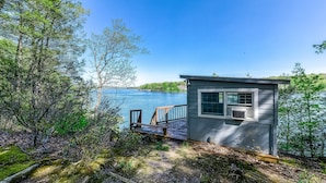Une petite cabane avec un quai s’avançant dans un lac, entourée d’arbres.