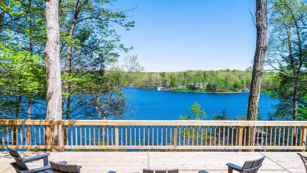 Une terrasse en bois avec des fauteuils Adirondack donnant sur un lac.