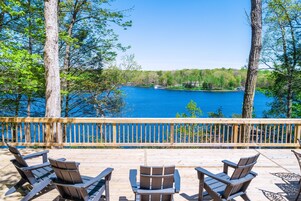 Una terraza de madera con sillas Adirondack con vistas a un lago.