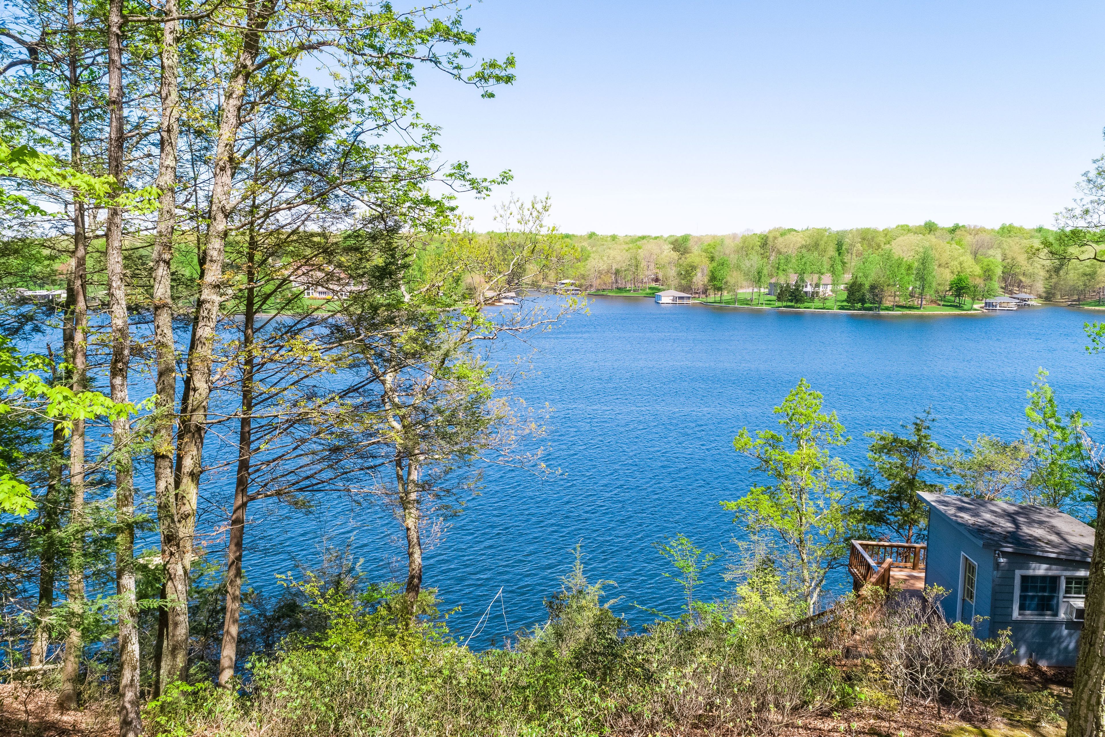 A lake surrounded by trees and a small cabin with a deck.