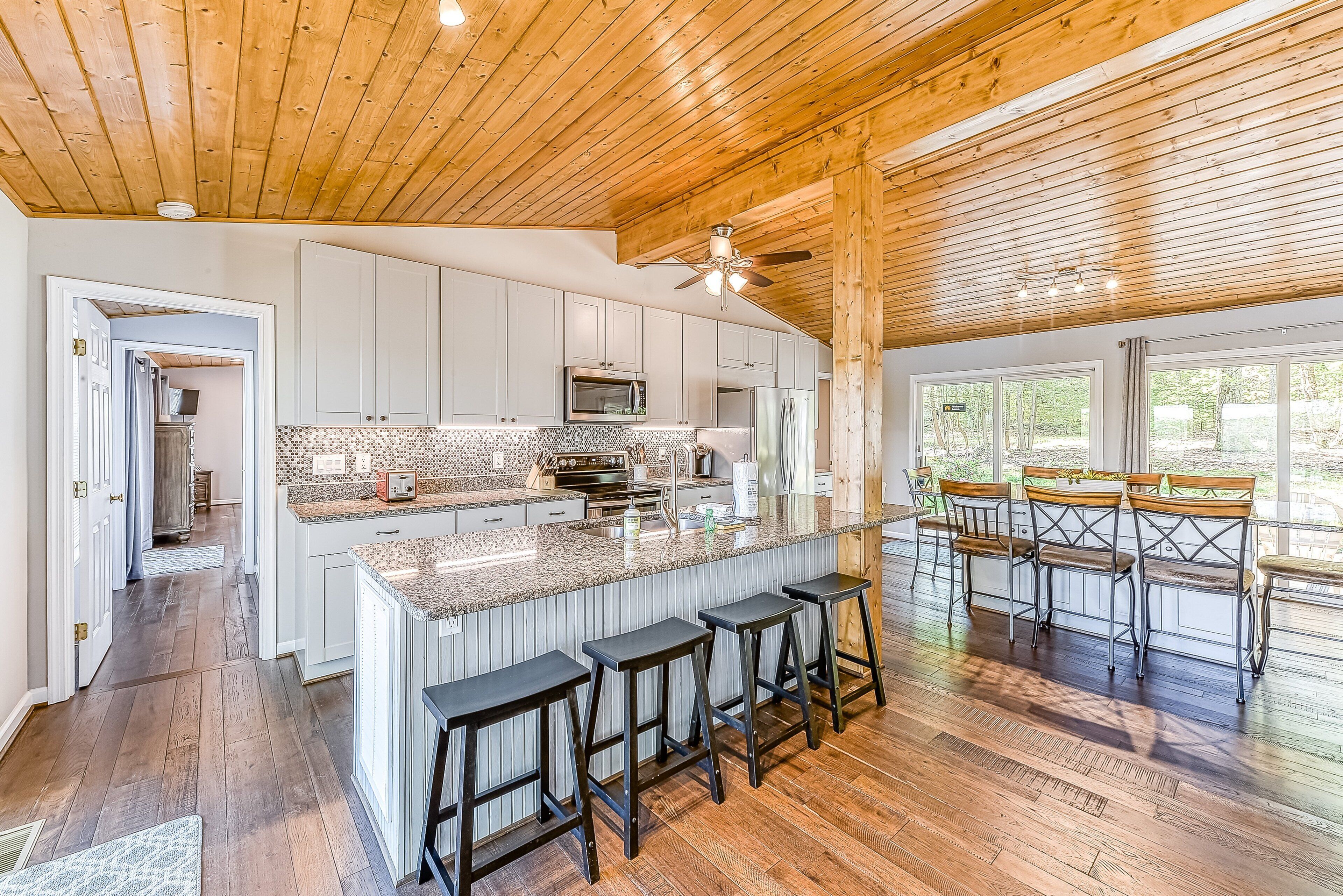 A spacious kitchen with a large island, wooden ceiling, and bar stools.