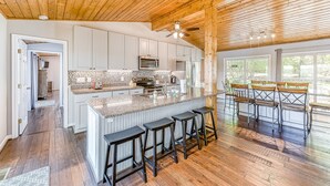 Une cuisine spacieuse avec un grand îlot central, un plafond en bois et des tabourets de bar.