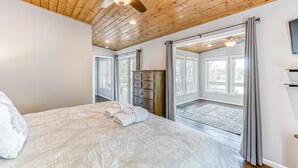 Une chambre à coucher avec un lit, un ventilateur de plafond, une commode et une vue sur l’extérieur grâce à de grandes fenêtres.