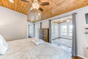 Ein Schlafzimmer mit einem Bett, einem Deckenventilator, einem Schminktisch und Blick ins Freie durch große Fenster.