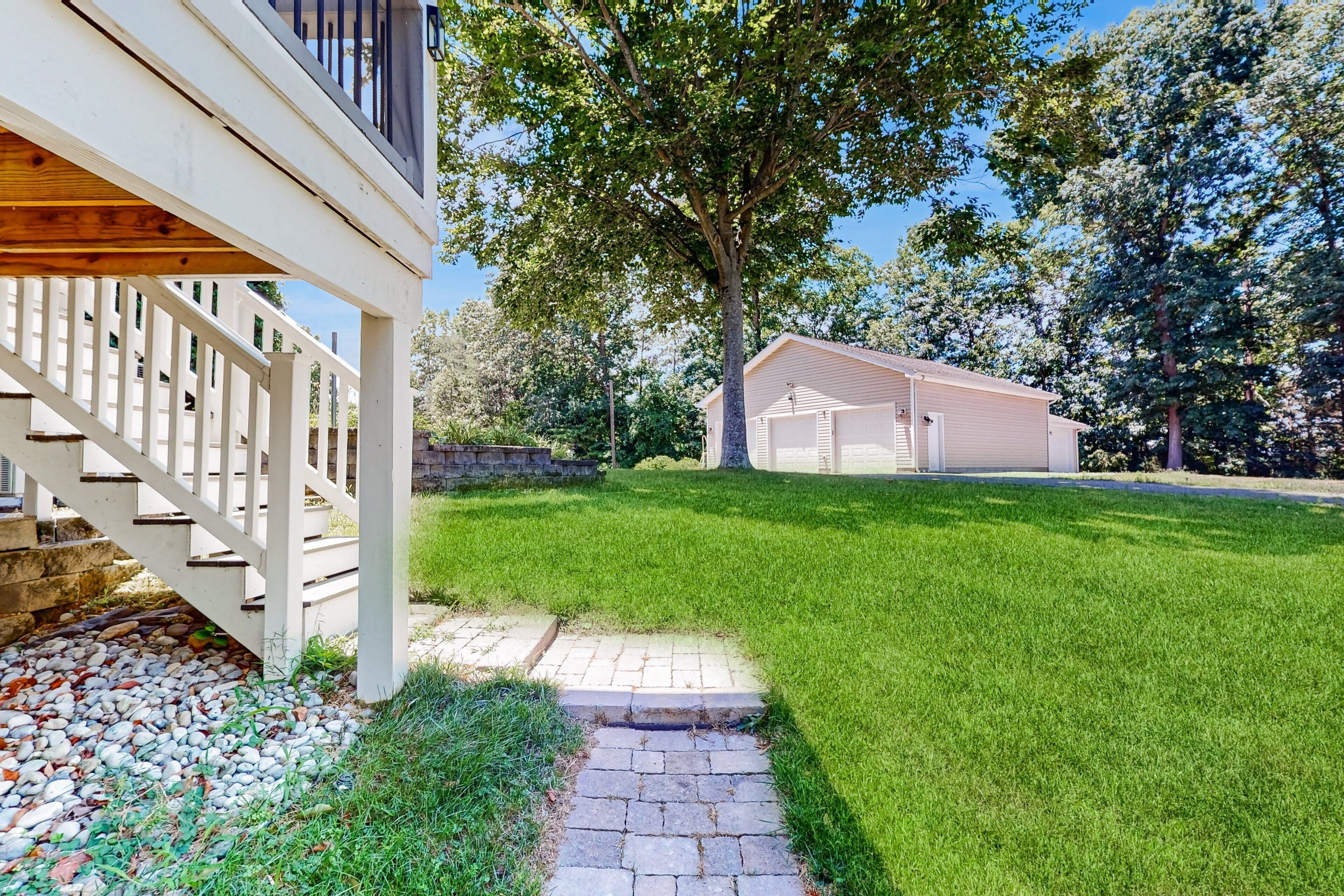 A residential property with a wooden deck, a stone pathway, a well-maintained lawn, and a garage.