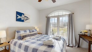A hotel room with a large bed, a window with curtains, a desk with a lamp, and artwork on the wall. - Peaceful Lakeside Retreat With hot Tub, Private Pool, Dock & Paddle Boards (Orange)