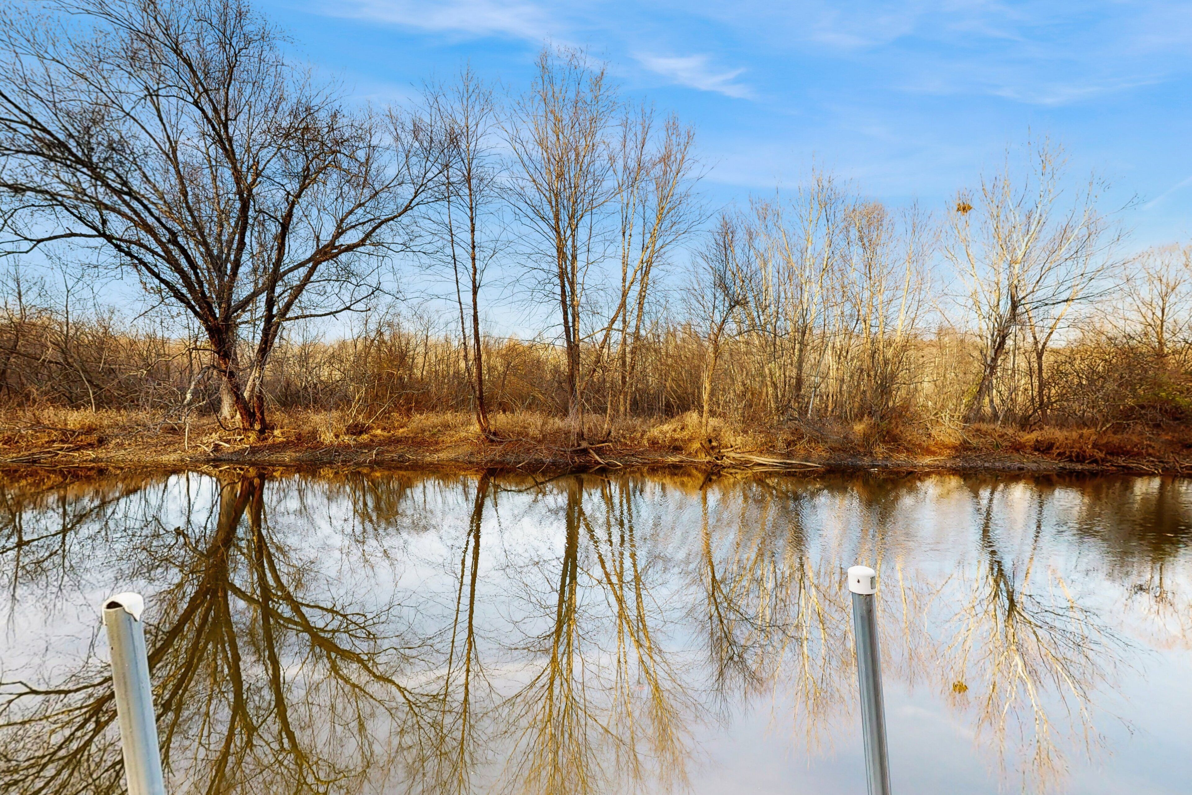Un río tranquilo con reflejos de árboles, cielo despejado y un embarcadero con un poste.