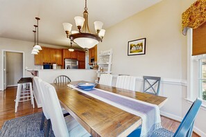 A dining area with a wooden table, chairs, a chandelier, and a kitchen in the background. - Peaceful Lakeside Retreat With hot Tub, Private Pool, Dock & Paddle Boards (Orange)