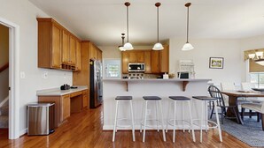 A modern kitchen with wooden cabinets, stainless steel appliances, and a bar area with stools. - Peaceful Lakeside Retreat With hot Tub, Private Pool, Dock & Paddle Boards (Orange)