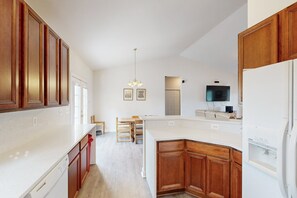 A kitchen with wooden cabinets, a white countertop, a built-in dishwasher, and a television mounted above the counter. - Two-story, Lakefront Getaway With Dock, Beach, Grill, 2 Kayaks, 2 Canoes, AC (Orange)