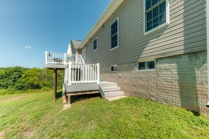 A two-story house with a balcony, a brick wall, and a grassy yard. - Two-story, Lakefront Getaway With Dock, Beach, Grill, 2 Kayaks, 2 Canoes, AC (Orange)