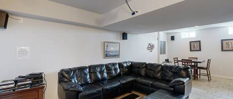 A living room with a black leather sofa, a wooden cabinet, a projector, and a dining area with a table and chairs.