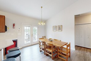 A dining area with a wooden table and chairs, a hanging light fixture, a fire extinguisher, and a door leading to an outdoor area. - Two-story, Lakefront Getaway With Dock, Beach, Grill, 2 Kayaks, 2 Canoes, AC (Orange)