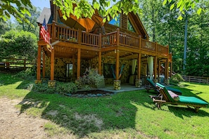 Une cabane en bois dotée d’un balcon, d’un drapeau et de deux fauteuils de jardin.