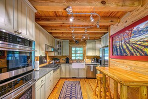 A kitchen with wooden ceilings, stainless steel appliances, and a large window. - Luxurious Lakefront Cabin With hot Tub, Game Room, & Washer/dryer- dog Friendly (Bumpass)