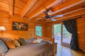 A wooden cabin bedroom with a bed, a ceiling fan, a painting, and a view through a glass door. - Luxurious Lakefront Cabin With hot Tub, Game Room, & Washer/dryer- dog Friendly (Bumpass)