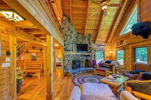 A log cabin interior with a stone fireplace, wooden furniture, and a television. - Luxurious Lakefront Cabin With hot Tub, Game Room, & Washer/dryer- dog Friendly (Bumpass)
