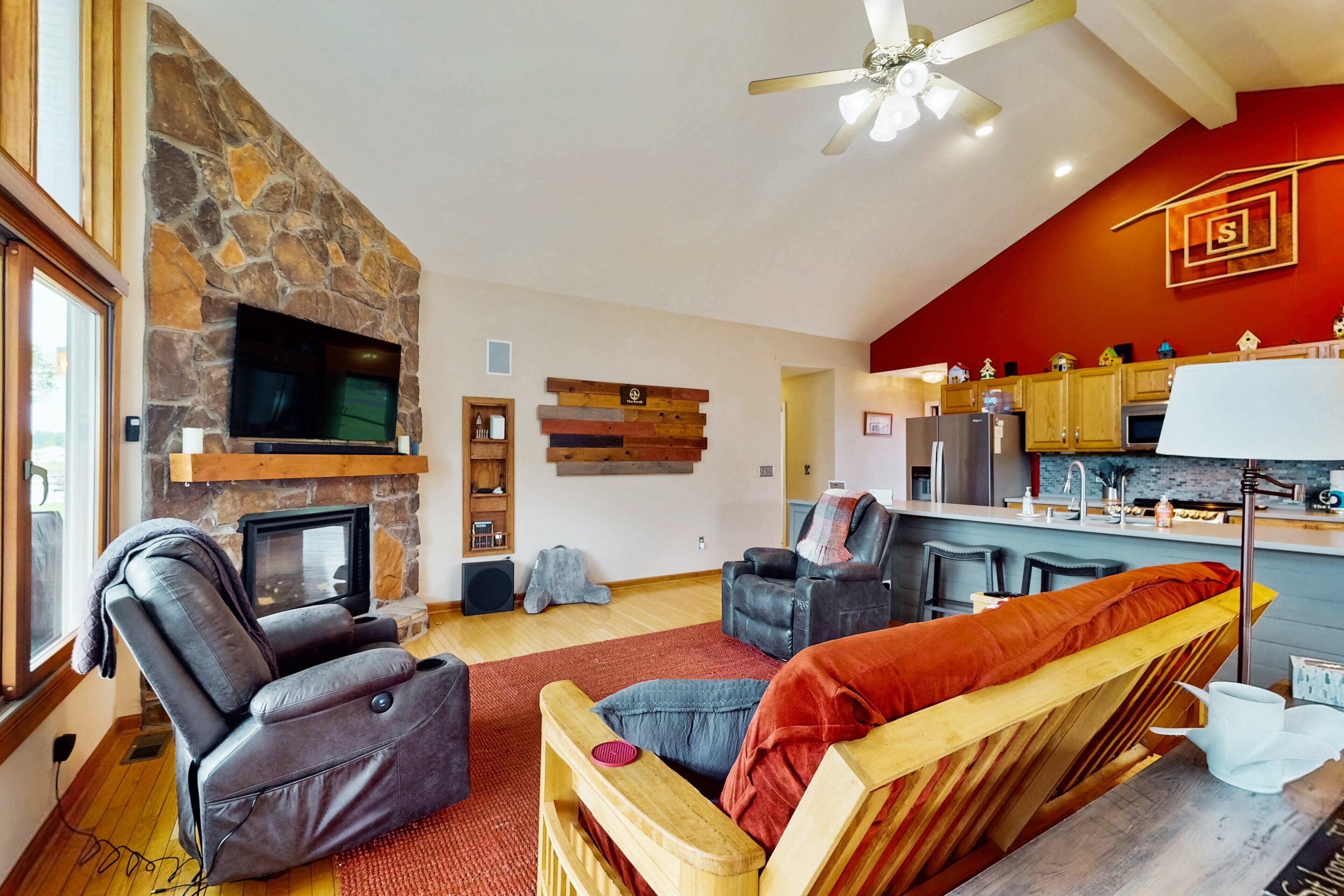 A living room with a stone fireplace, a television, a recliner, and a bar area.