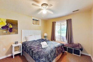 A hotel room with a bed, a ceiling fan, a nightstand, a window with curtains, and a view of the outdoors. - Spacious Lakefront House W/patio, Balcony, Grill & Foosball (Mineral)