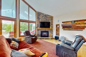 A living room with a stone fireplace, a television, and a wooden wall decor. - Spacious Lakefront House W/patio, Balcony, Grill & Foosball (Mineral)