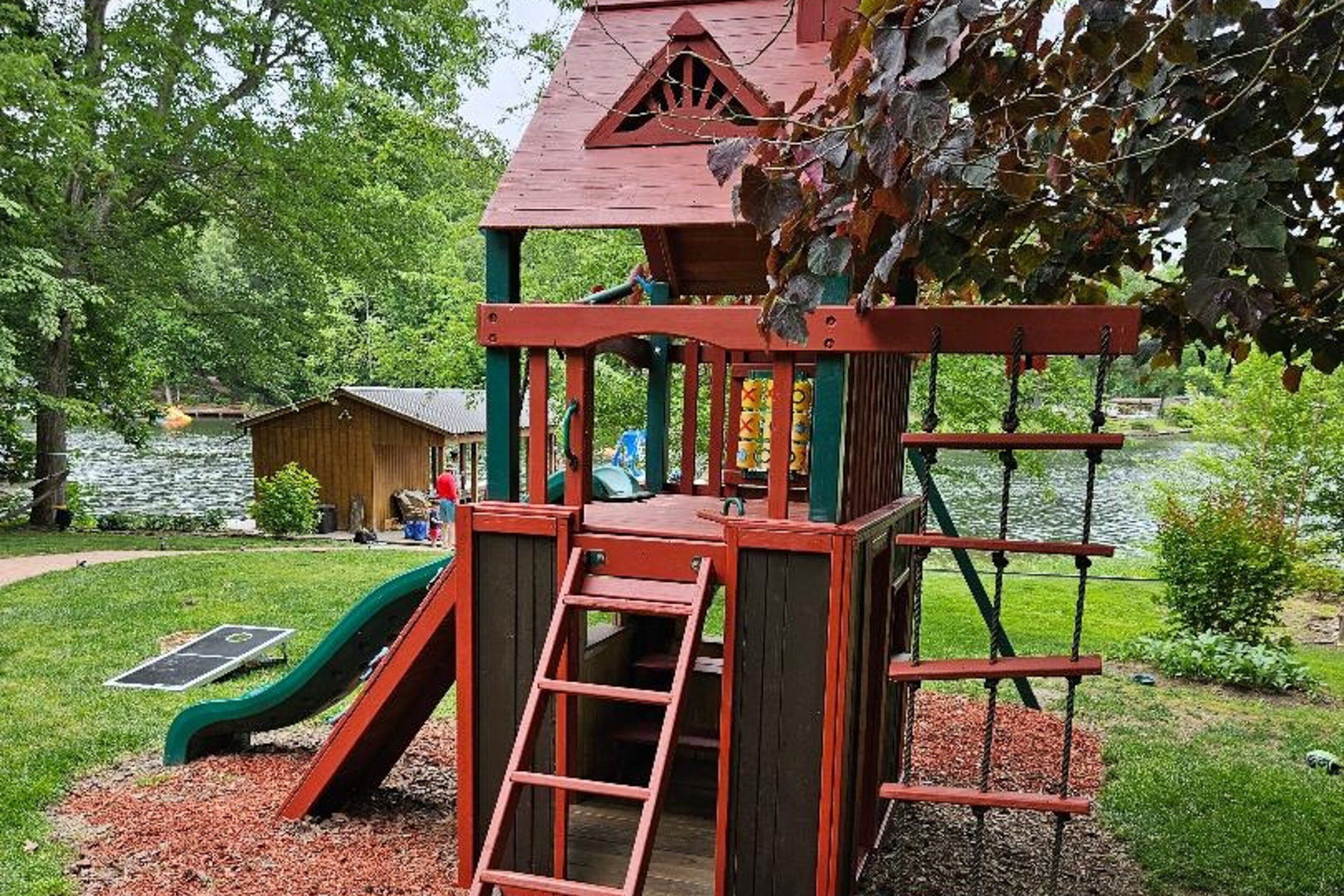 A playground with a slide, climbing net, and a small building structure.