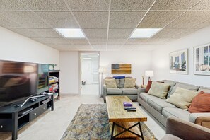 A living room with a TV, sofa, coffee table, and a patterned rug. - Tranquil Lakefront Retreat With hot Tub, Screened Porch, Kayaks, and More (Bumpass)