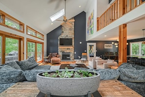 A spacious living room with a stone fireplace, large windows, and a high ceiling. - Stunning Lakefront House With View, Free Wifi and Secluded Swimming Area (Spotsylvania)