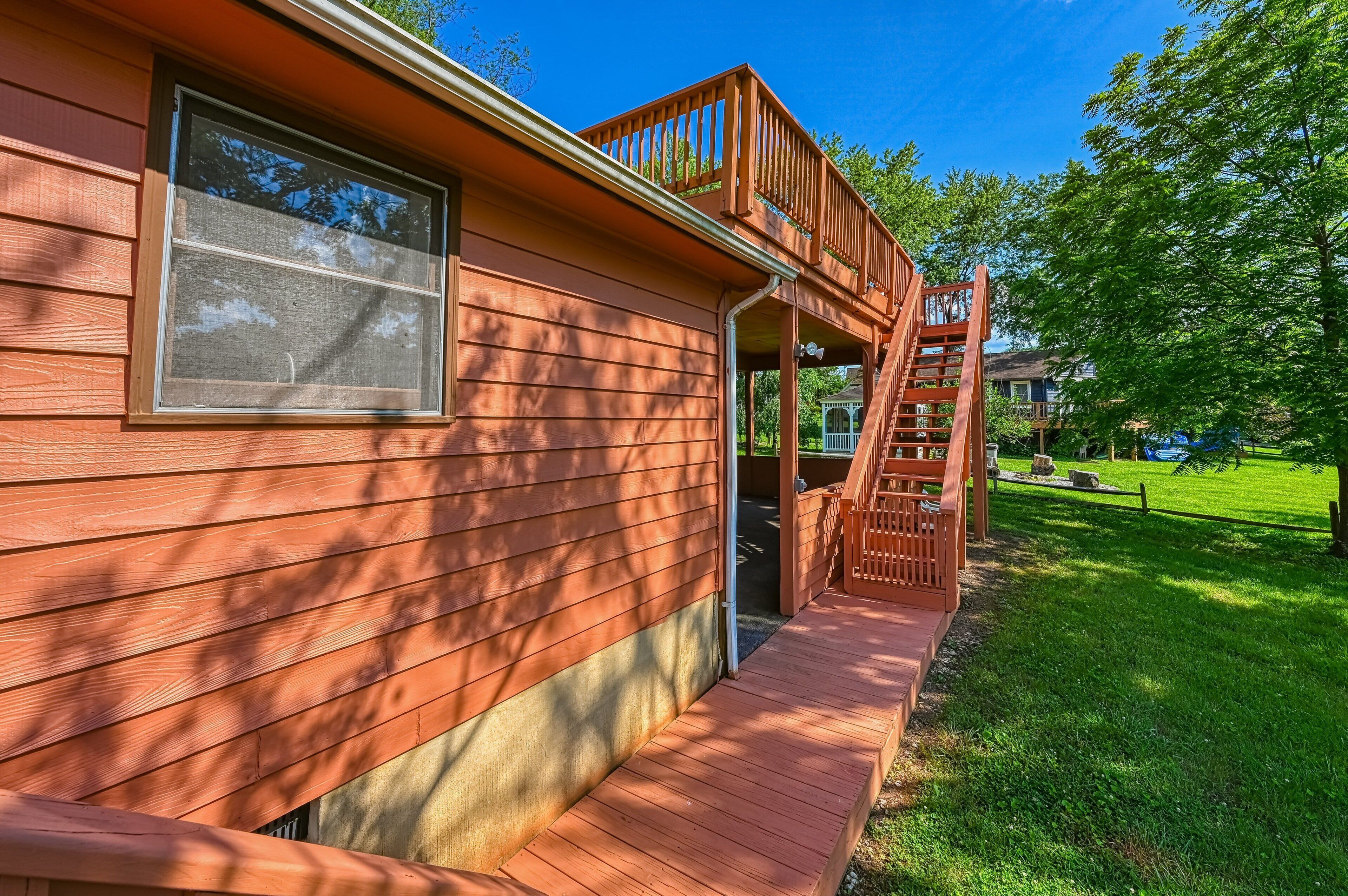 A wooden house with a porch, a staircase, and a grassy yard.