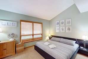 A bedroom with a bed, a wooden cabinet, a fan, a window with blinds, a nightstand with a lamp, and framed pictures on the wall. - Lakefront Retreat With Views, hot Tub, Kid's Play Area, Dock & Fiber Internet (Mineral)