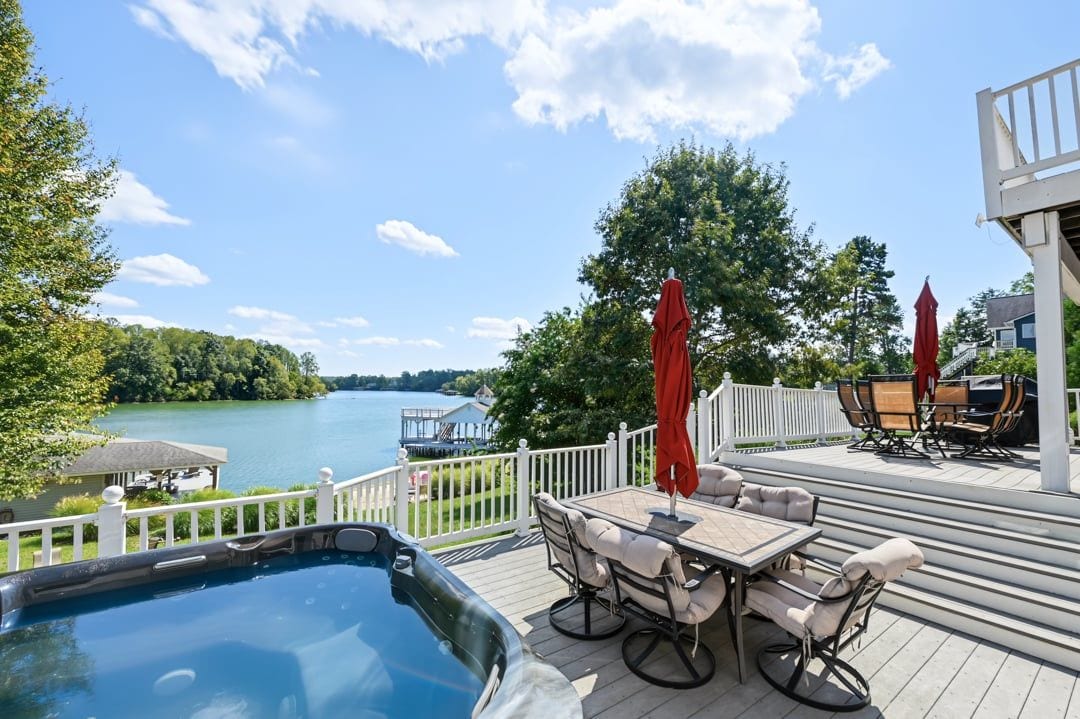 A deck with outdoor furniture, a hot tub, and a view of a lake.