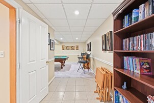A hallway with a pool table, chairs, and a bookshelf filled with books.