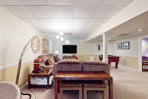 A living room with a sofa, a coffee table, a TV, and a foosball table. - Lakefront Retreat With Views, hot Tub, Kid's Play Area, Dock & Fiber Internet (Mineral)