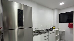A modern kitchen with a stainless steel refrigerator, a gas stove, a sink, and white cabinetry.