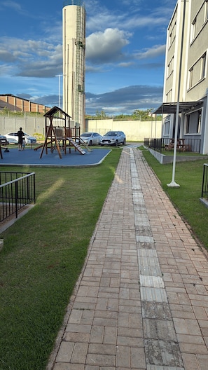 Un camí pavimentat, un parc infantil i cotxes aparcats en una zona residencial.