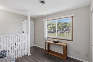 Ein Zimmer mit Holzboden, weißer Geländer, einem Fenster mit Seeblick und einem kleinen Holzkonsolentisch.