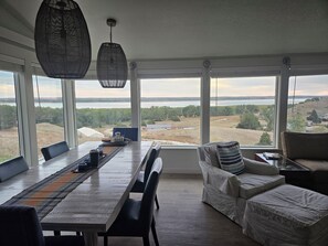 A dining area with a view of a lake, large windows, and a hanging light fixture. - Relaxing 5-bedroom house with one of the best views at Lake Mac. (Brule)