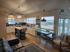 A modern kitchen with a dining area, a sofa, and a view of the outdoors.