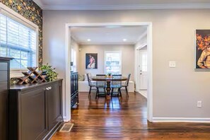 A dining area with a wooden floor, a dining table with chairs, and a kitchen area with dark cabinetry. - Fuzzy Peach Bungalow: Huge Yard w/fire pit. Pet Friendly! (Atlanta)