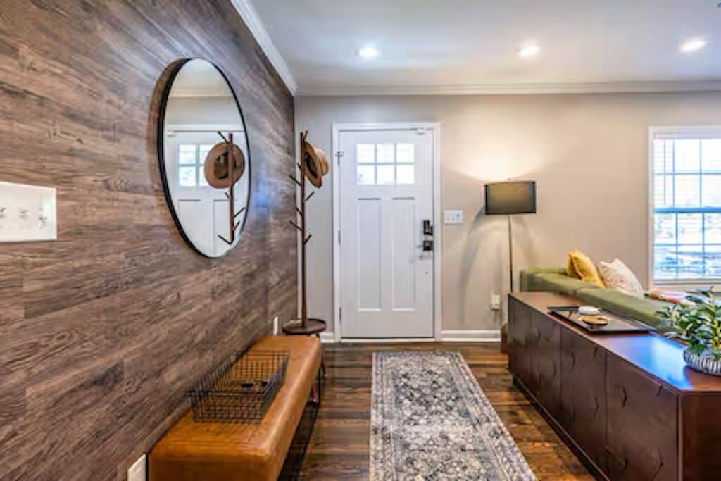 A room with a wooden wall, a bench, a sofa, a TV, and a door.