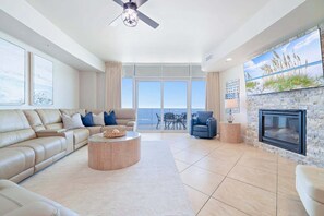 Ein geräumiges Wohnzimmer mit einer Ledersofa, einem runden Couchtisch, einem blauen Sessel, einem Kamin und einem Balkon mit Meerblick.