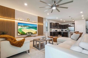 A modern living room with a flat-screen TV, a ceiling fan, and a kitchen area. - Disney Dream Home | Mario, Frozen & Minions (Davenport)