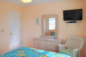 Ein Schlafzimmer mit Bett, Kommode, Stuhl, Fernseher und einer Tür.