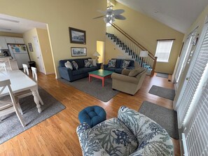 A living room with a sofa, a coffee table, a dining table with chairs, a staircase, and a kitchen area. - Canal-front 3 Bed 2 Bath home including a dock. (Holden Beach)